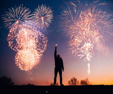 Man with a firework in his hand while fireworks are exploding in the air