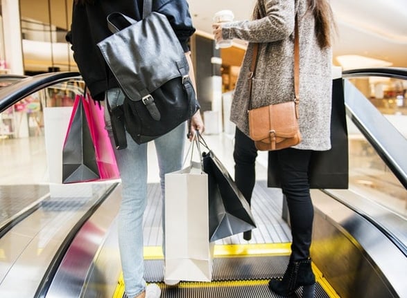 shoppers holding bags riding an escalator 